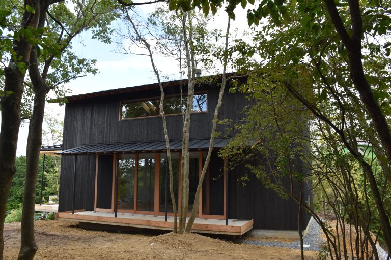 Completed Kato Villa rear exterior, Awajishima — charred black timber cladding, timber deck and full-height glazing set among mature trees