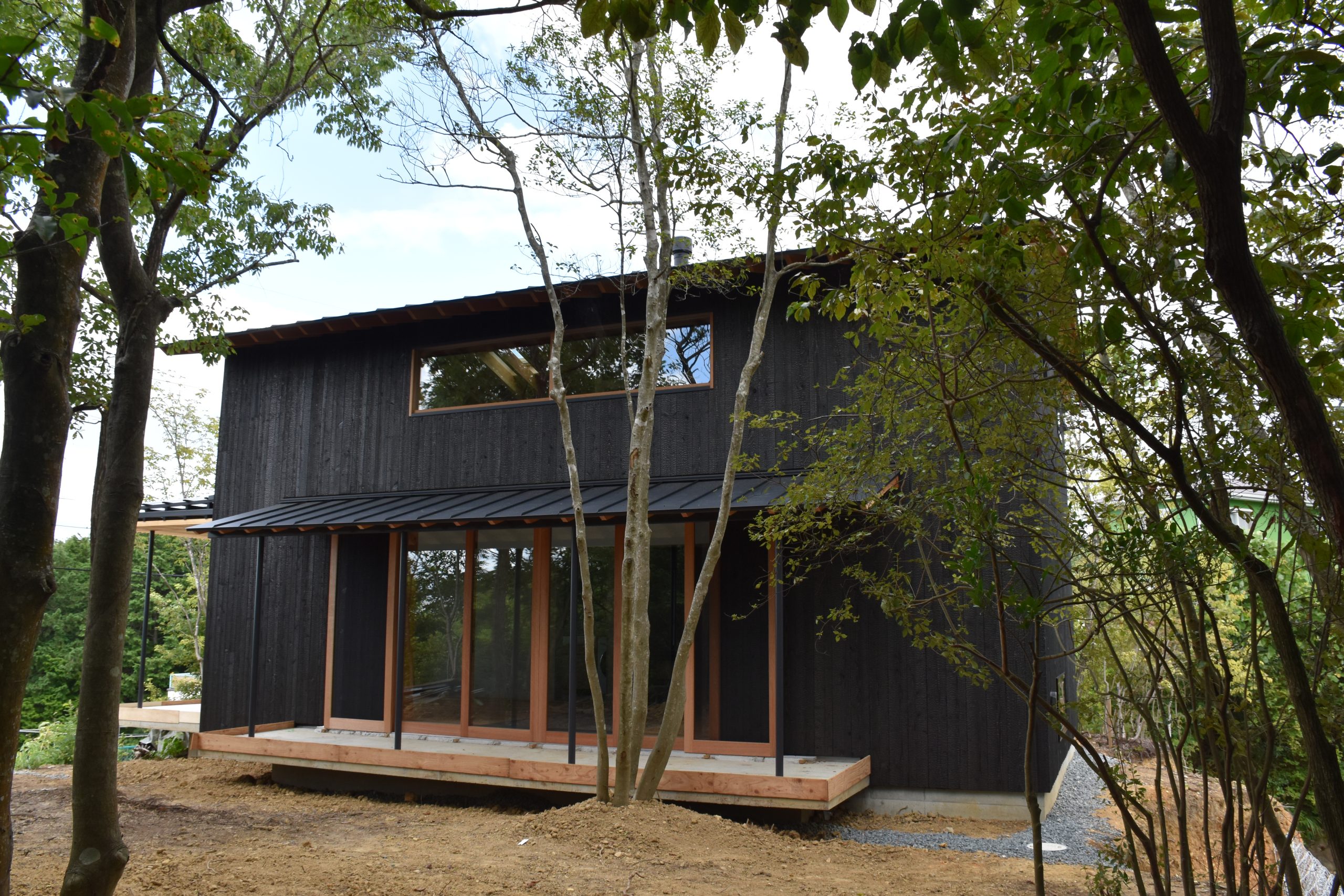 Completed Kato Villa rear exterior, Awajishima — charred black timber cladding, timber deck and full-height glazing set among mature trees