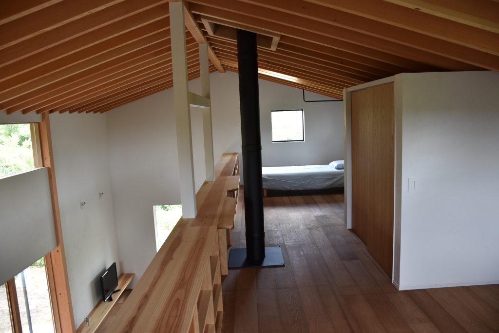 Kato Villa upper loft level showing exposed timber rafter ceiling, timber floor, steel flue column and bedroom beyond mezzanine balustrade