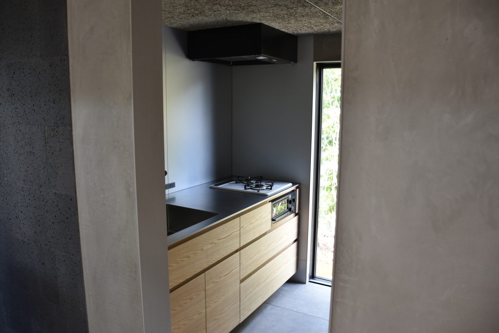 Kato Villa kitchen viewed from living area — timber cabinetry, concrete wall finish and garden window