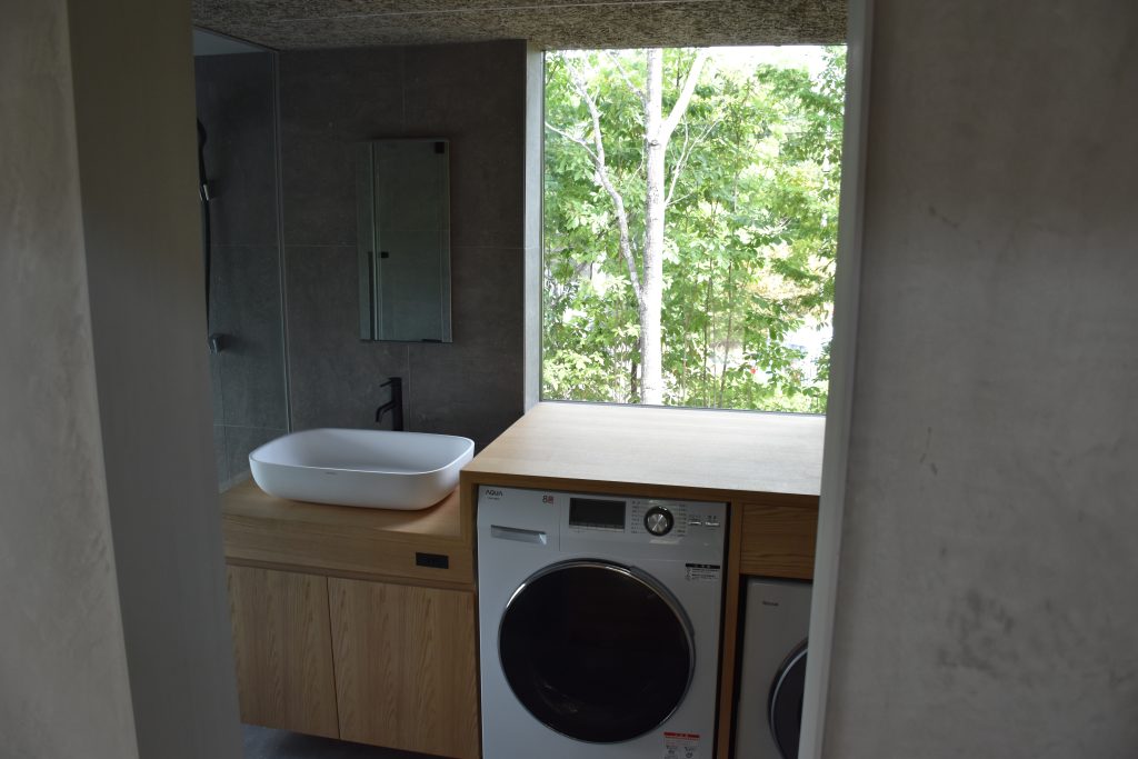 Kato Villa bathroom and laundry — vessel basin on timber vanity, washer-dryer unit and concrete wall finish with garden window