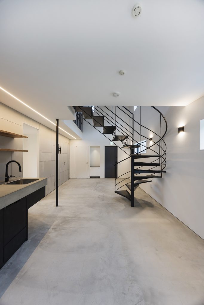 Completed first floor open-plan interior at Sunset Villa, Awajishima — spiral staircase, concrete floor and kitchen viewed toward front entry