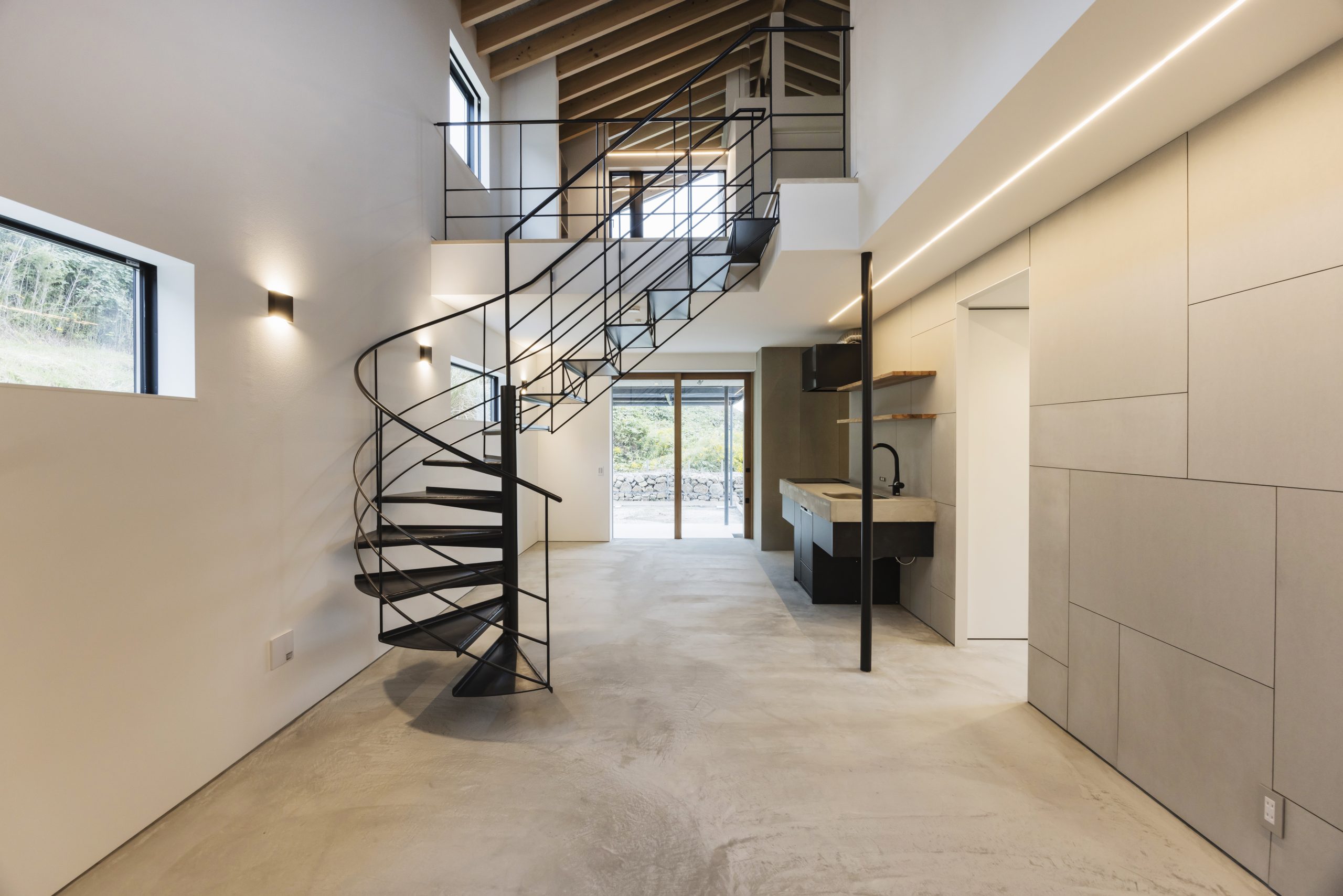 ull interior view of Sunset Villa from front door — spiral staircase, exposed rafter ceiling, concrete floor and kitchen beyond