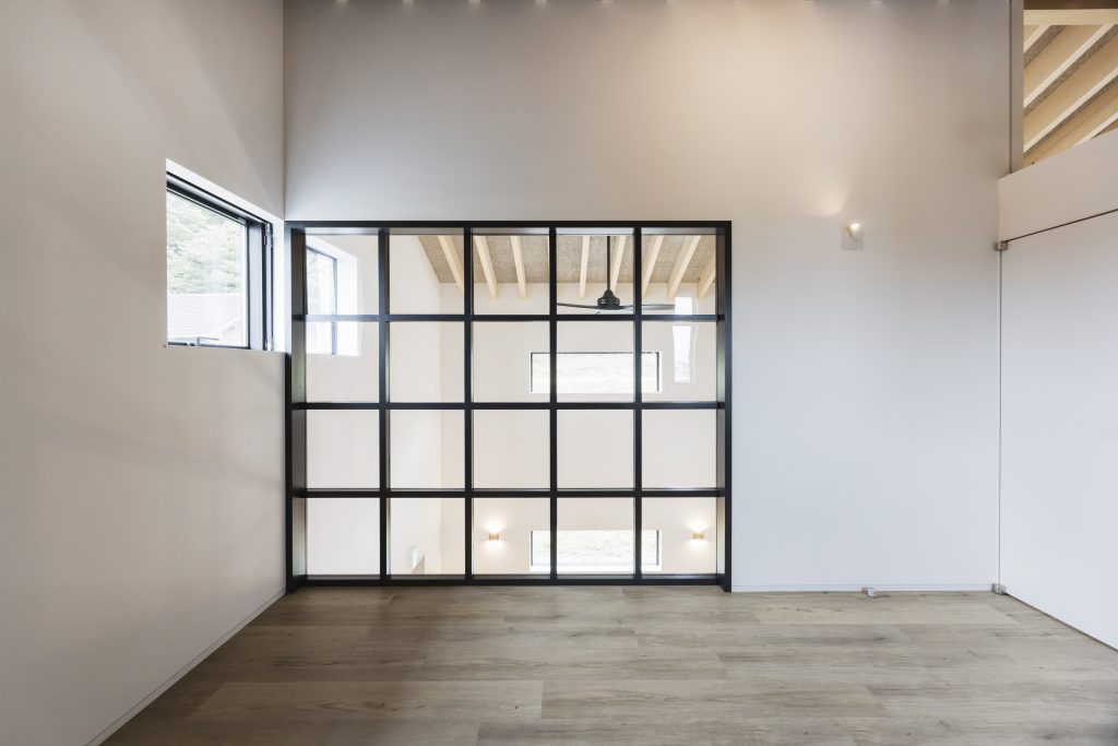 Children's room at Sunset Villa looking into double-height void through full-height steel-framed glazed internal wall with timber floor