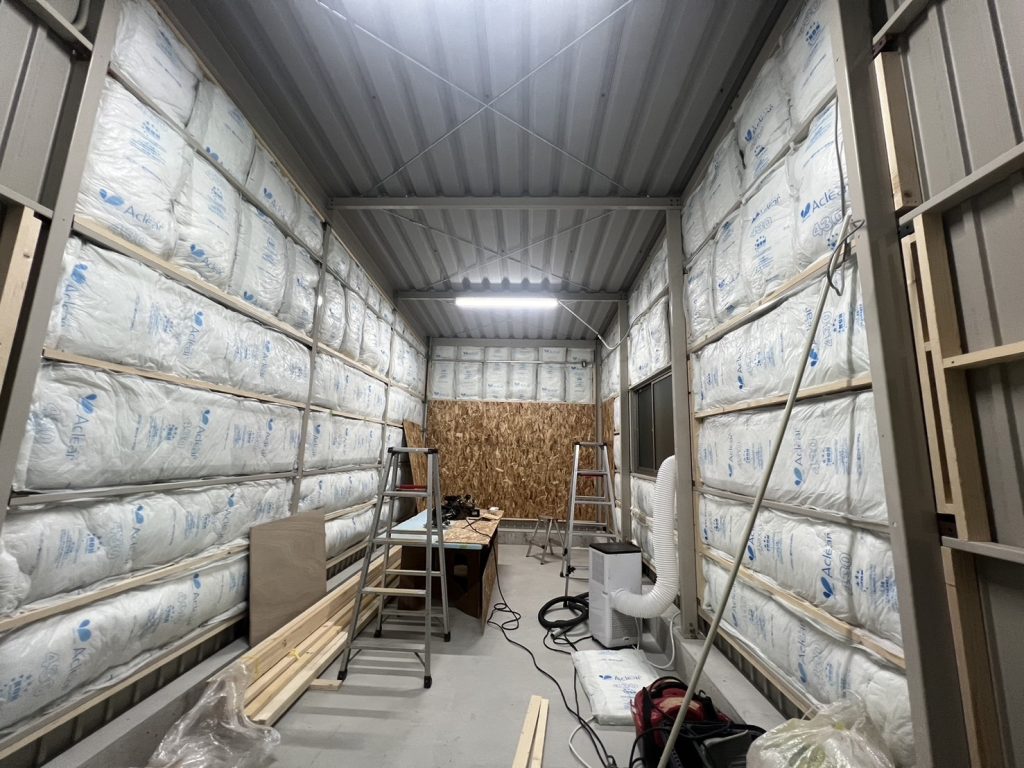 Insulation batts being installed to walls and ceiling of a Kakuichi steel garage during clubhouse conversion fit-out