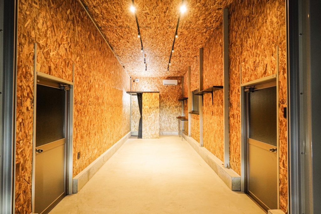 Interior corridor of a Japanese steel garage kit converted to a clubhouse in one week, OSB wall finish and track lighting throughout