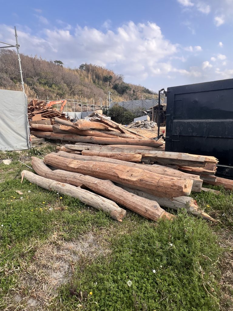 Salvaged kominka timber logs stockpiled on site following demolition — reclaimed structural timber for sustainable minka restoration and rebuild