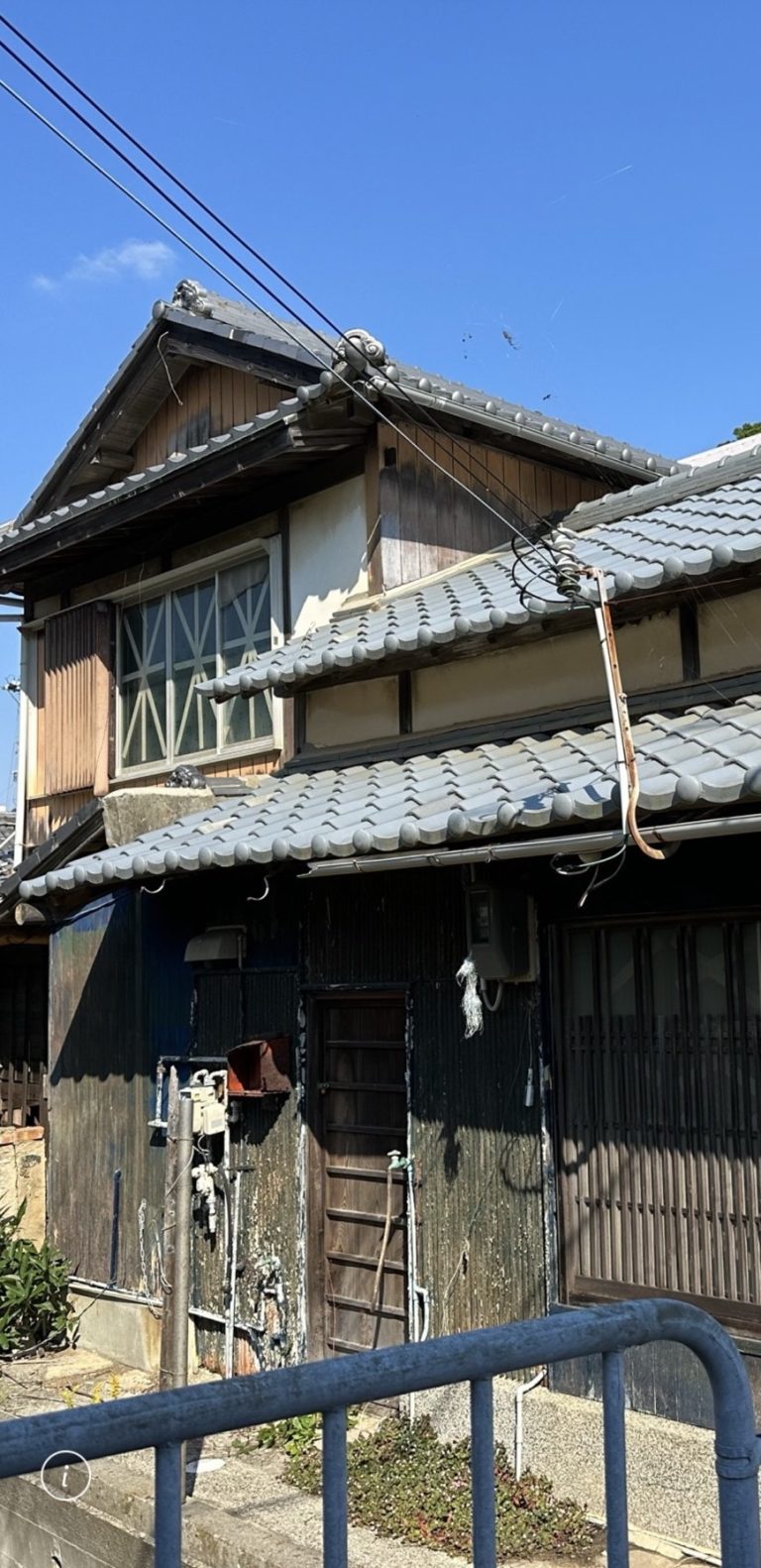 Weathered two-storey kominka exterior in a Japanese fishing village showing original tile roof and aged timber facade