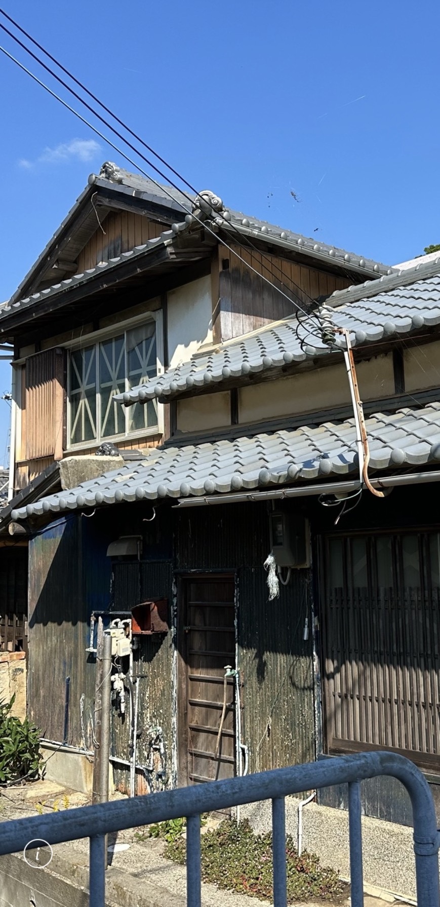 Weathered two-storey kominka exterior in a Japanese fishing village showing original tile roof and aged timber facade